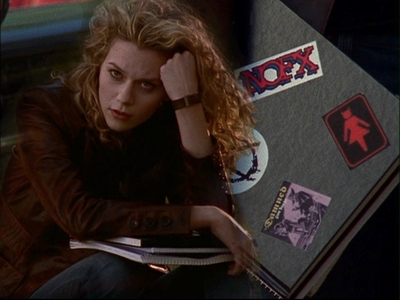  One of the stickers on her notebook is the band NOFX, and the A is for anarchy. The grey sticker appears to say "Damned", possibly (The) Damned. I'm not sure if the red woman with devil ears represent a band, ou what band that might be...